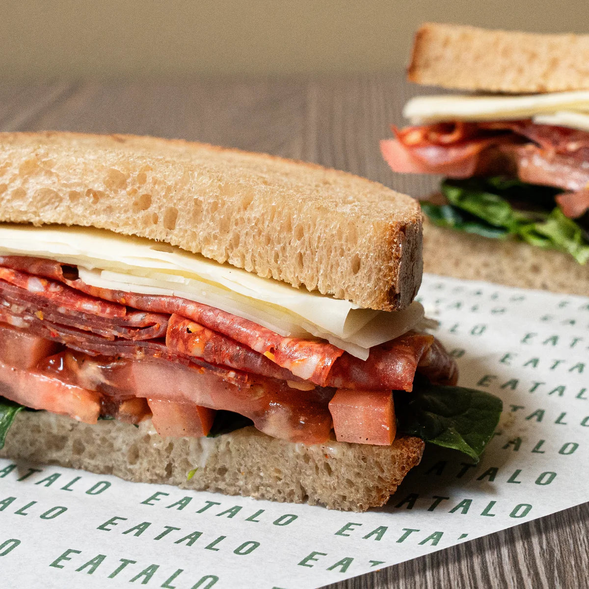 Sandwich with salami, cheese, and lettuce on a wooden surface with 'Eatalo' branding.