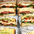 Multiple Italian sandwiches cut in half, stacked and wrapped in paper with visible text. Eatalo, in Sydney.