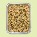 Foil pan of Italian tortellini pasta with peas and ham on a light green background