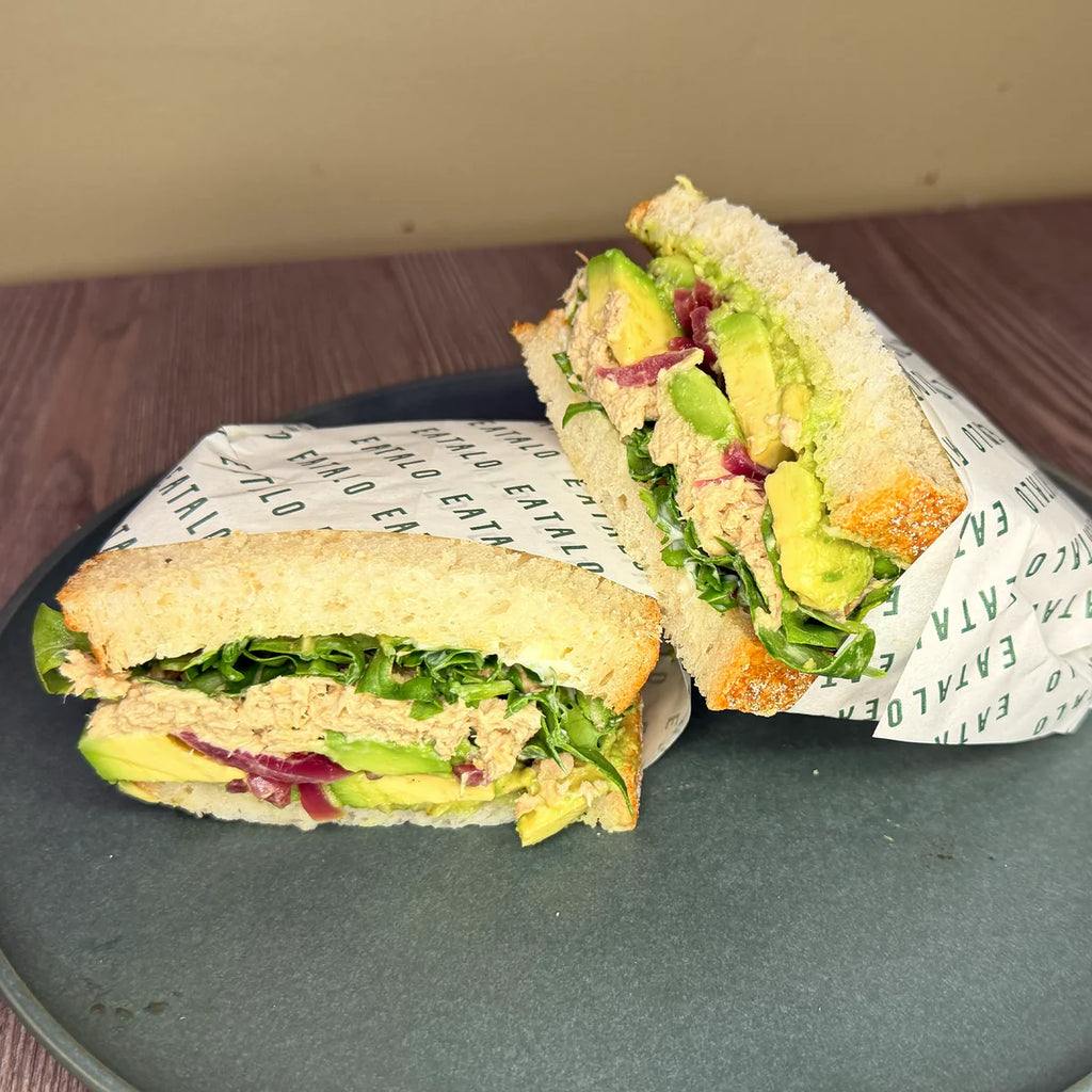 Half-cut sandwich with avocado and tuna on a plate with paper wrap.