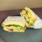Half-cut sandwich with avocado and tuna on a plate with paper wrap.
