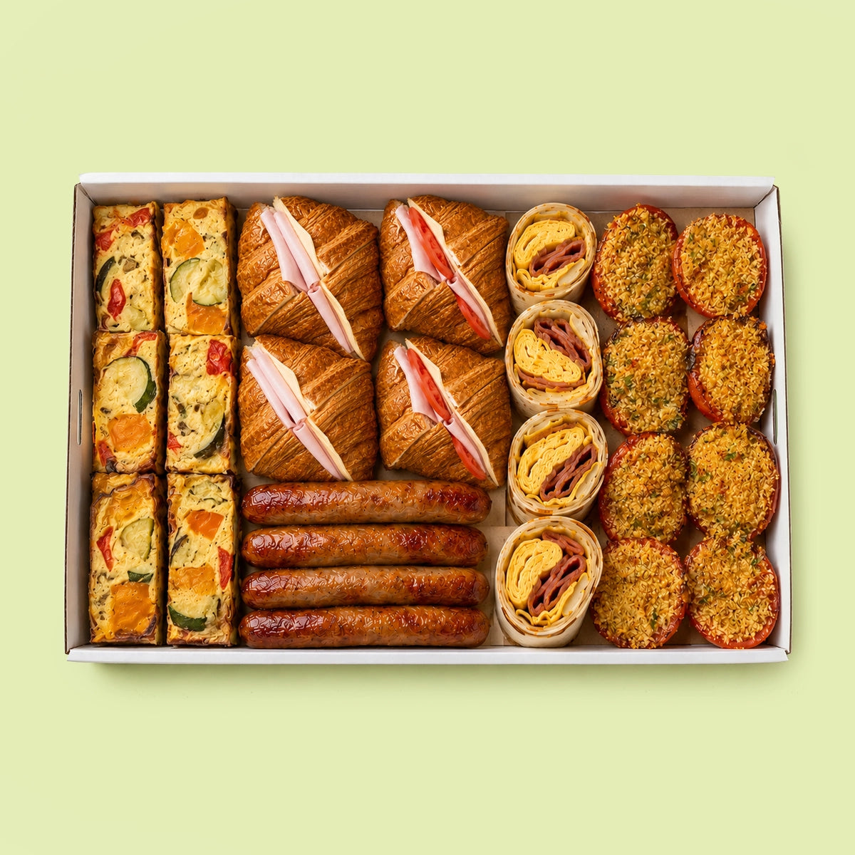 Assorted breakfast box with  food items including ham & cheese croissants, sausages, egg and bacon wraps, frittata and tomatoes gratin  in a box on a light green background